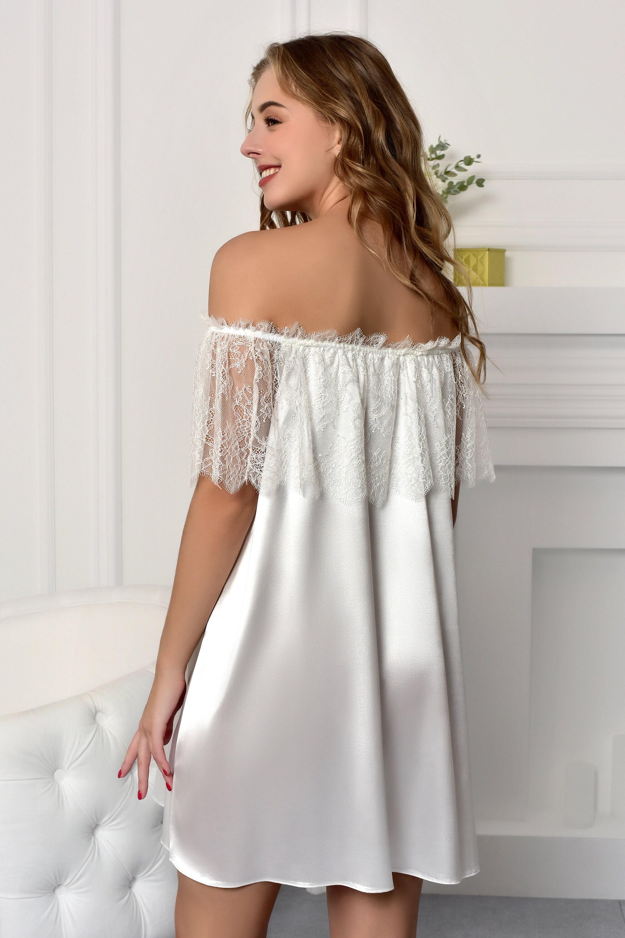 Woman wearing a white satin nightgown with lace details in a softly lit room.