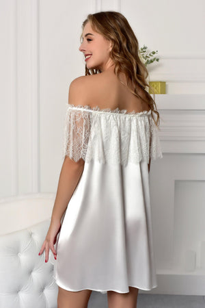 Woman wearing a white satin nightgown with lace details in a softly lit room.