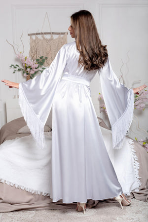 Woman in a white dress with fringe sleeves standing in a bedroom.