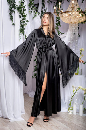 Woman wearing a black robe with fringes in an elegant room with white curtains and a chandelier.