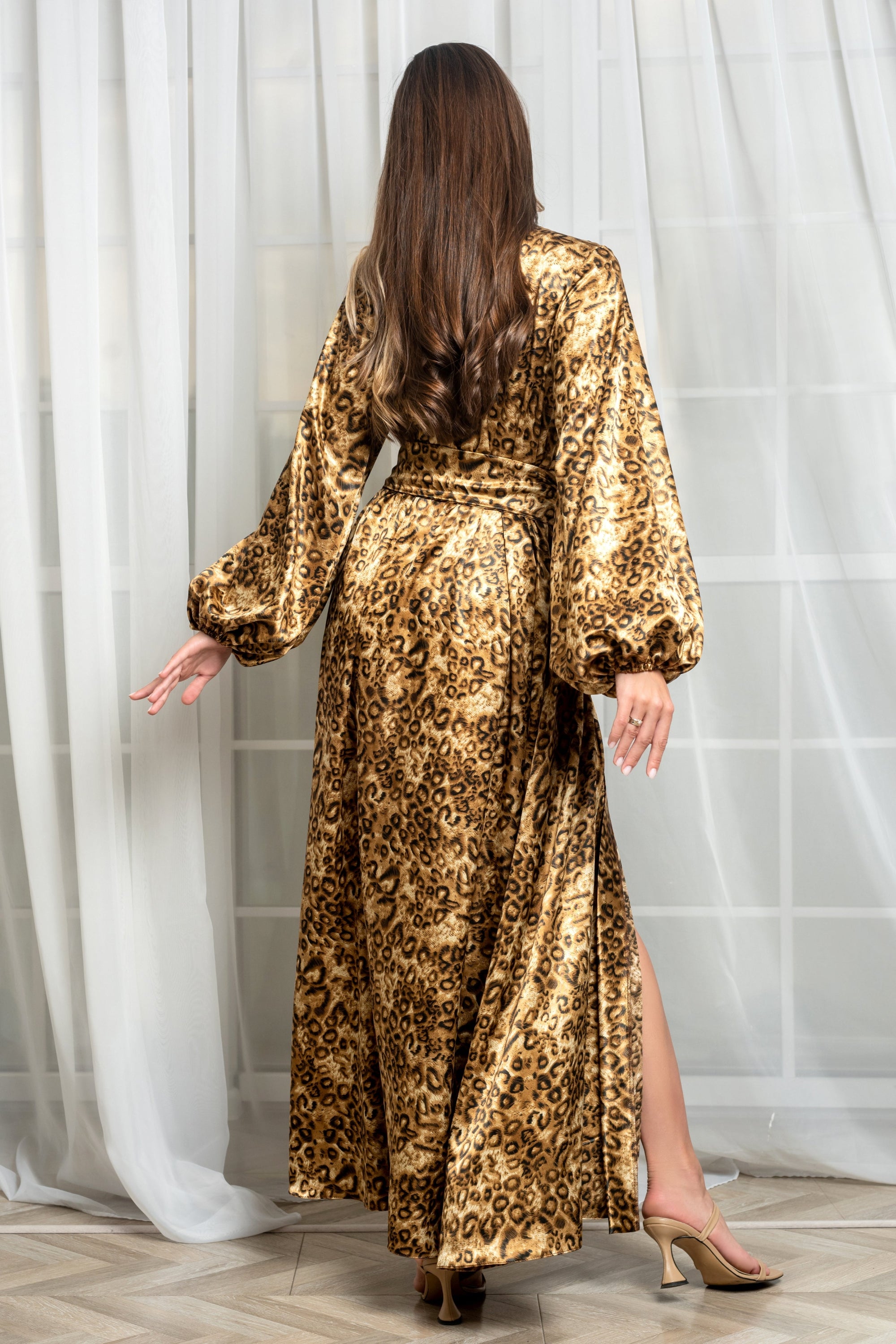 Woman wearing a gold leopard print dress with a white curtain background