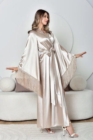 Woman wearing a long, flowing dress with fringe details in a modern interior setting.