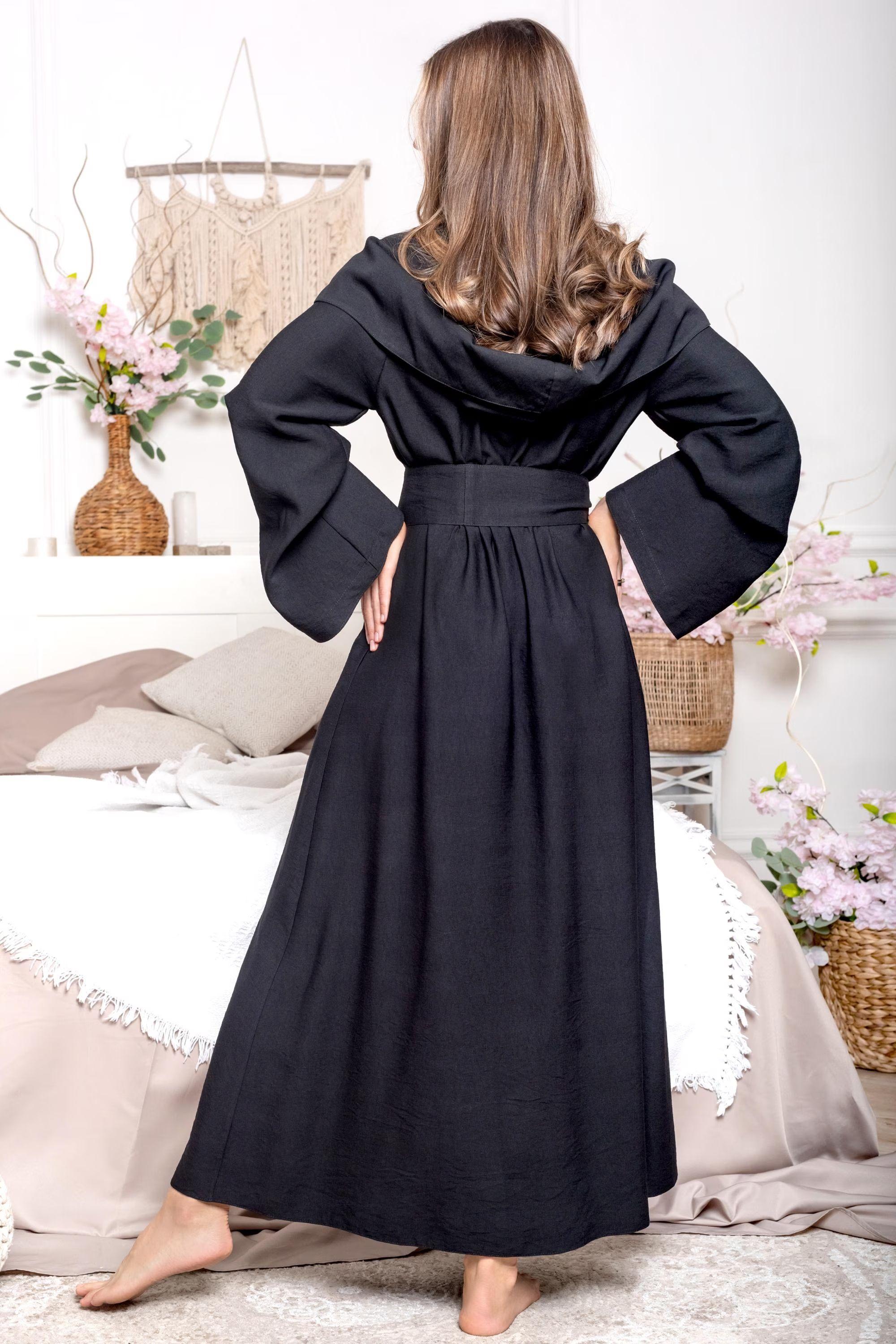 Woman wearing a black dress with wide sleeves in a bedroom setting