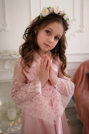Young girl in a pink dress with lace details and a floral headband indoors.