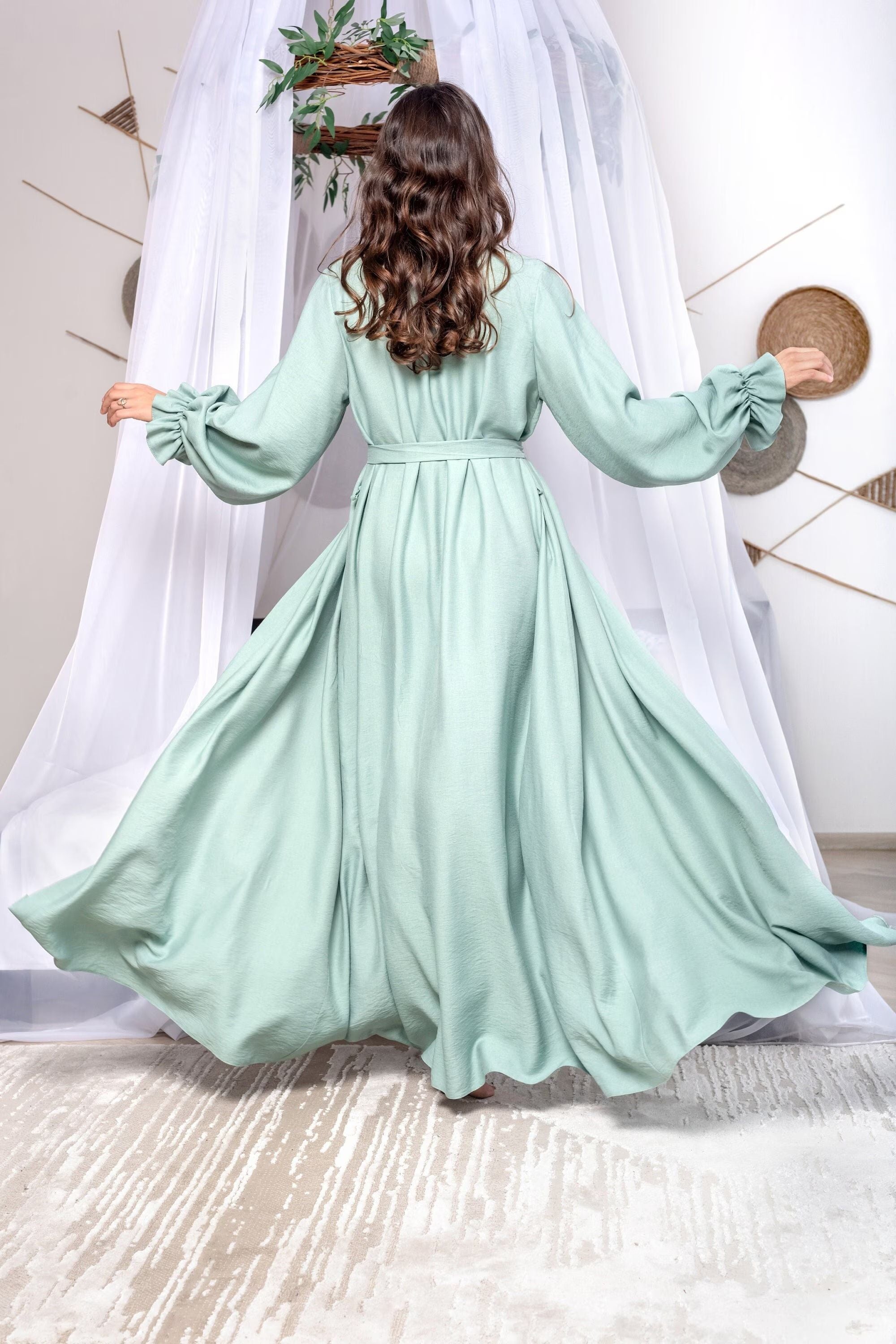 Woman wearing a light green dress with long sleeves in a minimalistic setting.