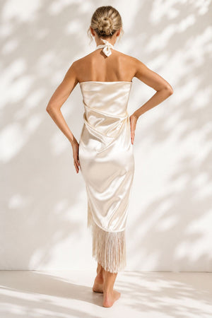 Woman wearing a strapless, off-white dress with fringe details against a white background