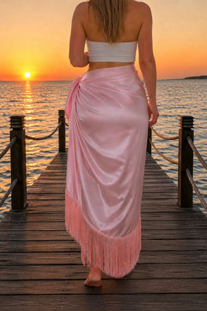Woman in a pink fringe skirt standing on a wooden dock at sunset.