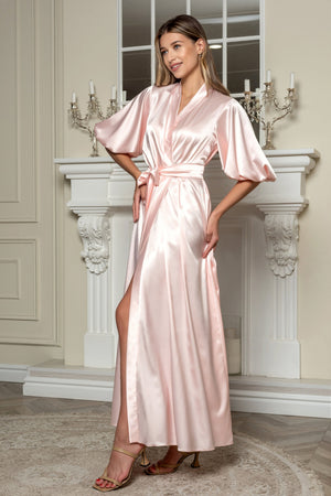 Woman wearing a pink satin robe in an elegant room with a fireplace.