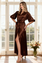 Woman in a brown satin dress standing in a bright room with large windows