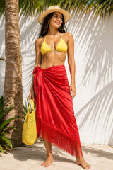 Woman in yellow bikini top and red sarong standing against a white wall with palm tree