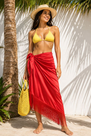 Woman in yellow bikini top and red sarong standing against a white wall with palm tree