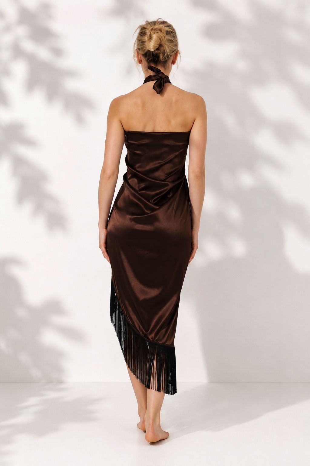 Woman wearing a brown strapless dress with fringe details against a white background