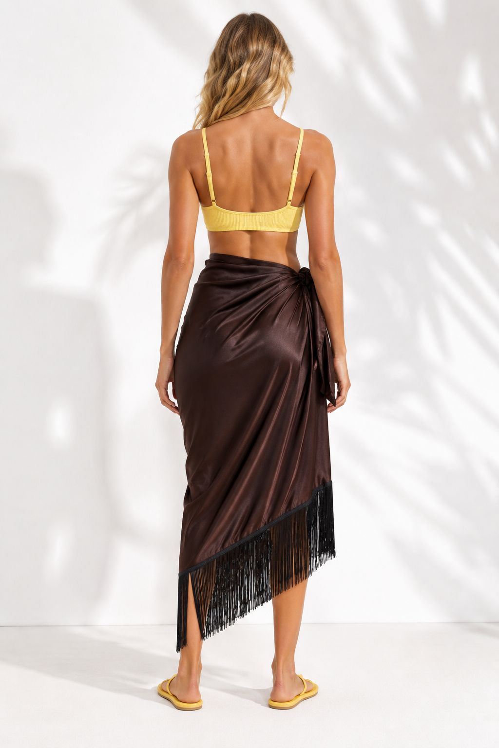 Woman wearing a brown sarong with fringe details on a white background