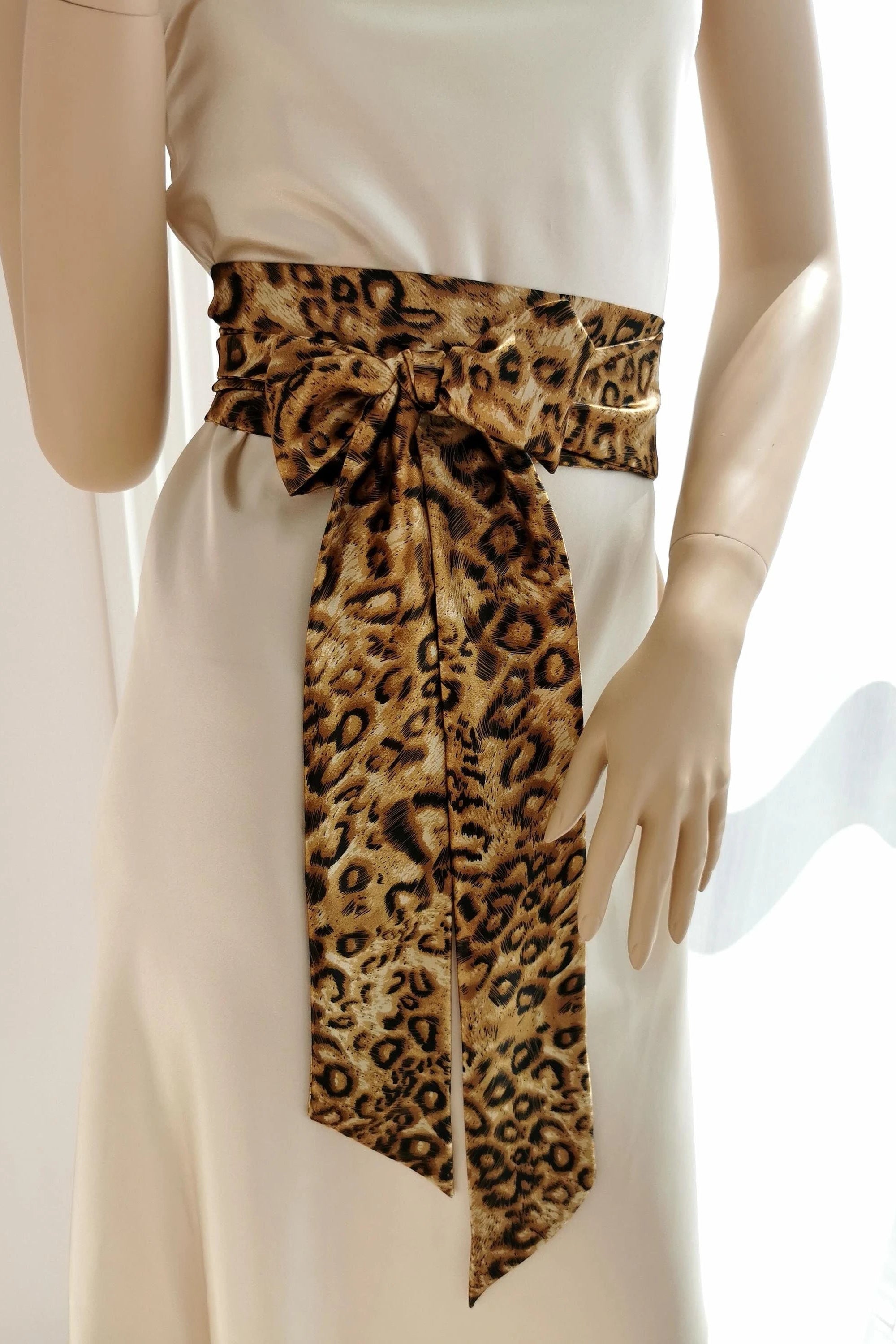 A leopard print satin sash belt tied in a bow on a mannequin wearing a white dress.