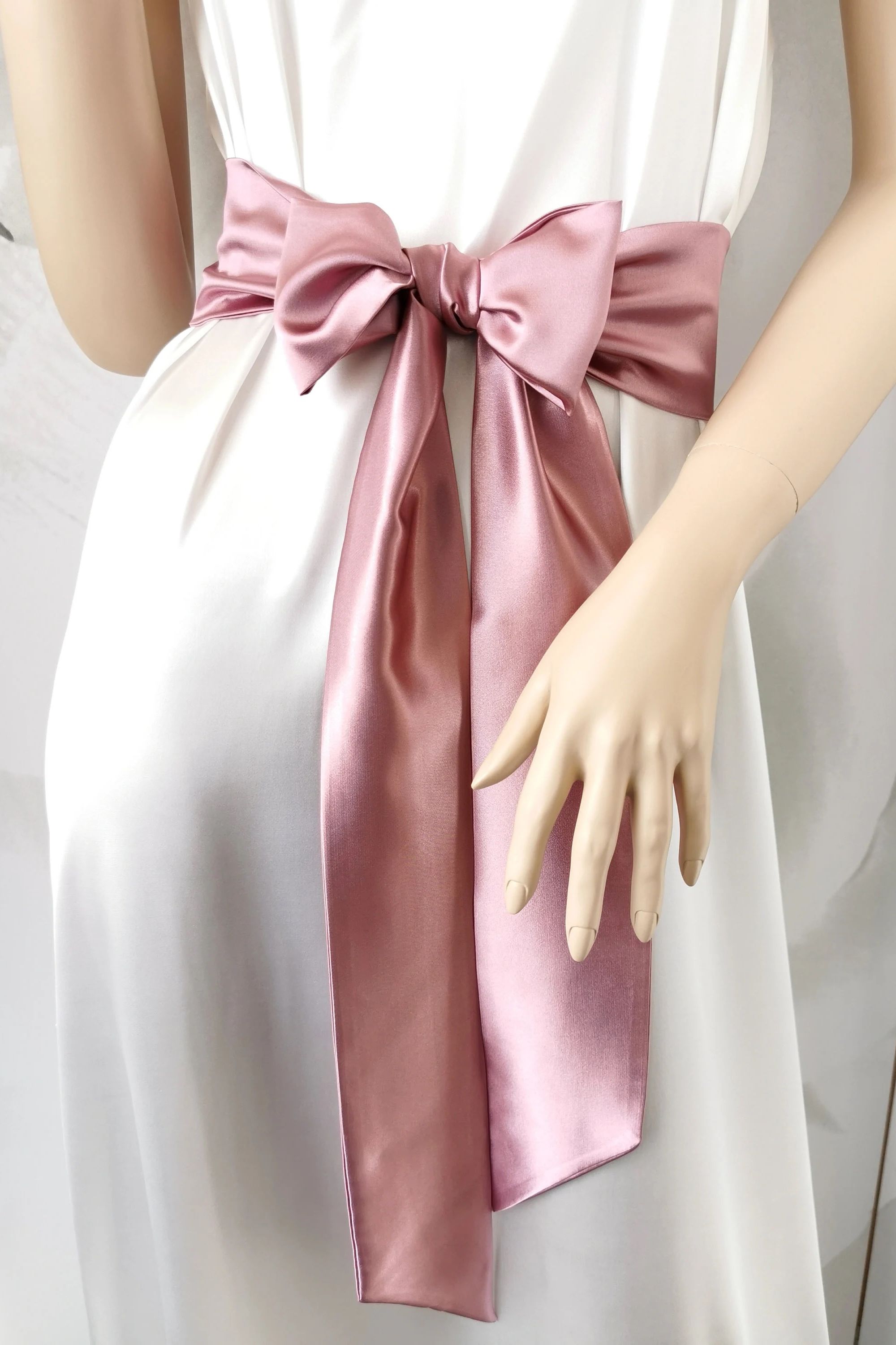 White dress with a large pink satin bow on a plain background