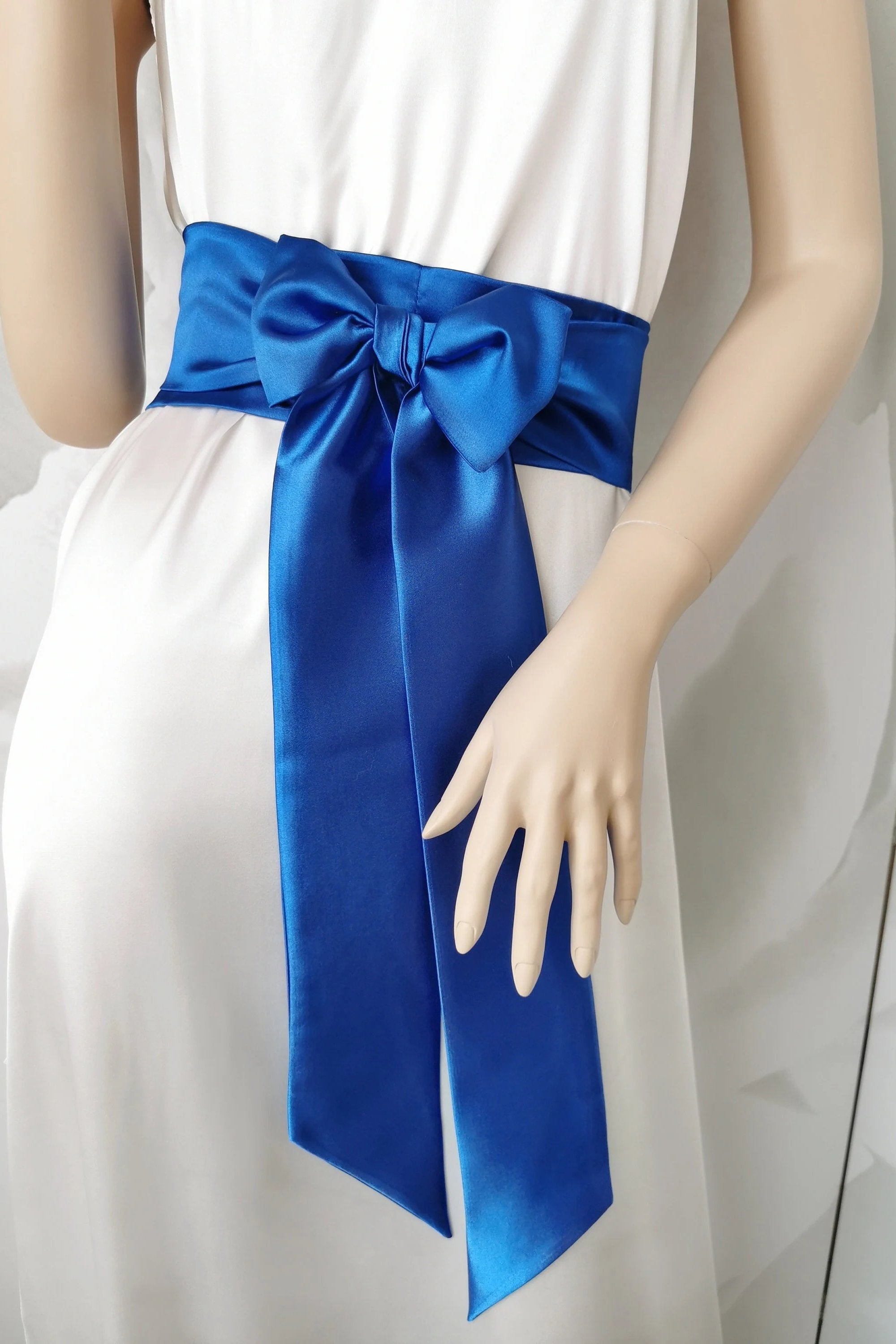 A dark blue satin sash belt tied in a bow, displayed on a mannequin wearing a white dress