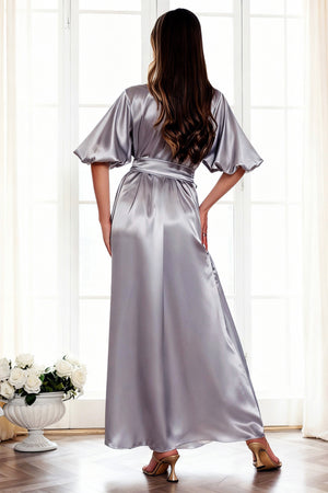 Woman wearing a silver satin robe standing in a bright room with large windows