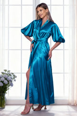 Woman wearing a blue satin robe standing in a bright room with large windows.