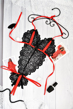 Black lace teddy lingerie with red ribbon bows and lace detailing, displayed on a white lace background with a photo and a pair of red heels.
