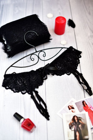 Black lace lingerie set on a white wooden surface with a red candle and nail polish bottle.