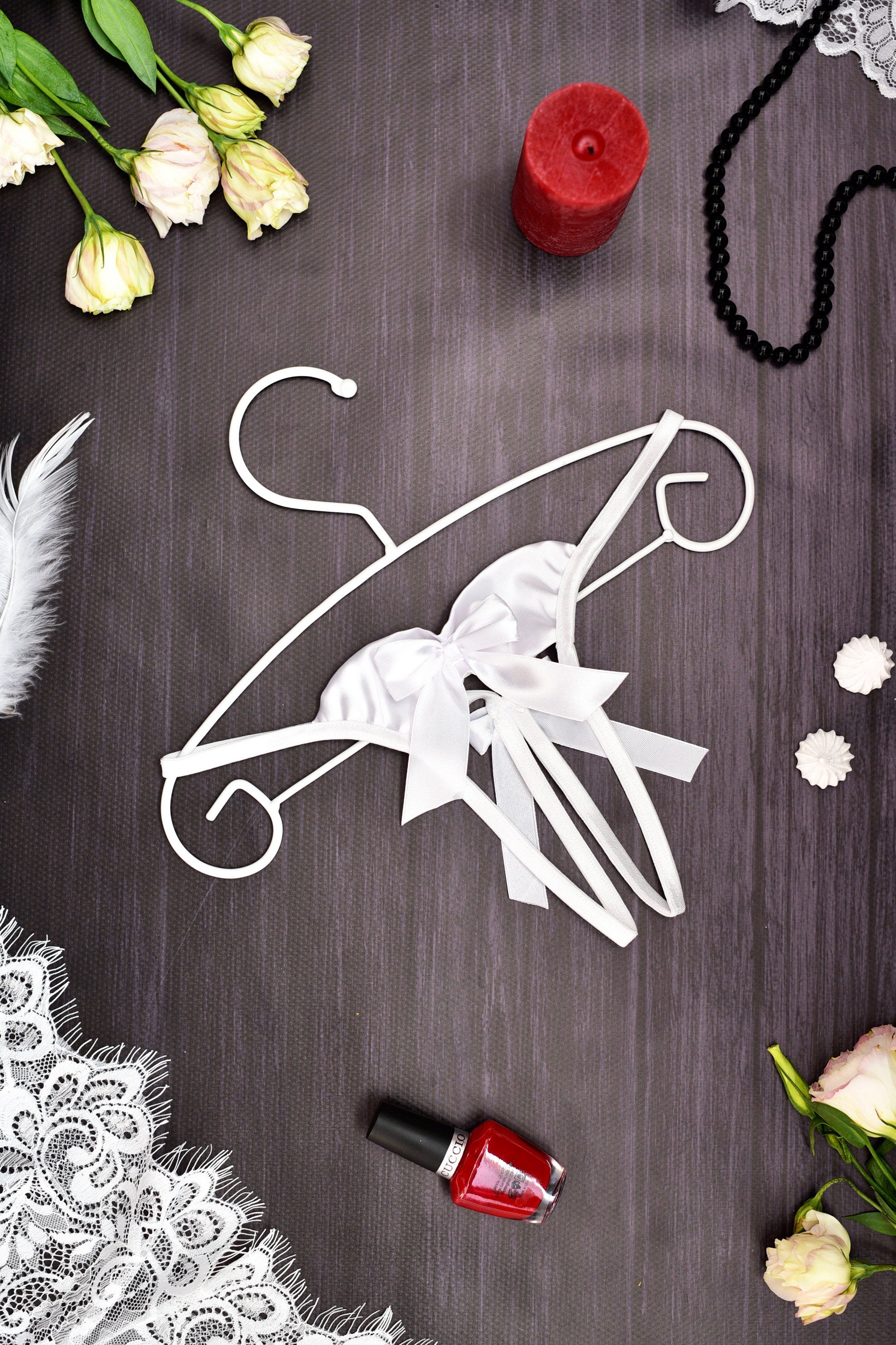 Decorative white hanger with bow on a dark surface with flowers and a candle.